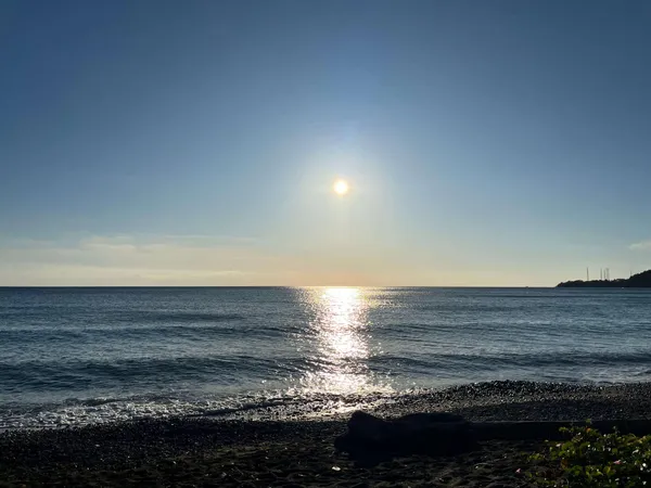 Soleil bas au-dessus d’une plage de galets, reflet doré sur l’océan